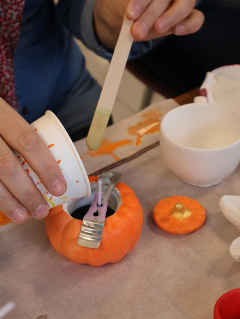 A person crafting a pumpkin candle with melted wax during a Halloween themed activity.